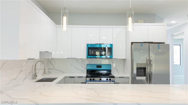 kitchen with white cabinets, decorative light fixtures, modern cabinets, a sink, and appliances with stainless steel finishes