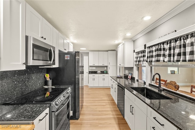 kitchen featuring light wood-type flooring, white cabinets, a sink, stainless steel appliances, and backsplash