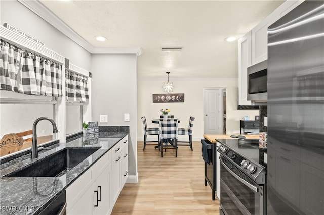 kitchen featuring white cabinets, a notable chandelier, a sink, ornamental molding, and stainless steel appliances