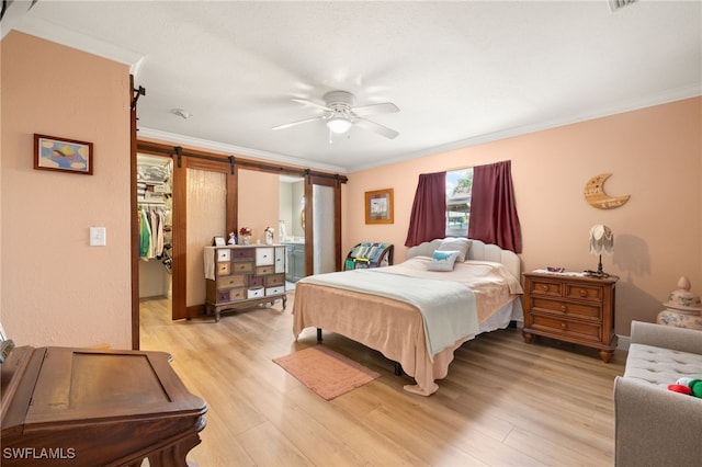 bedroom featuring crown molding, a walk in closet, a barn door, and light wood finished floors