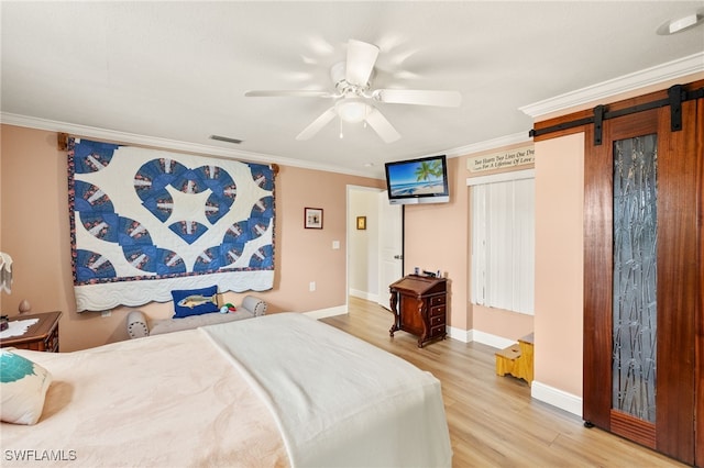 bedroom featuring visible vents, baseboards, a barn door, crown molding, and light wood finished floors