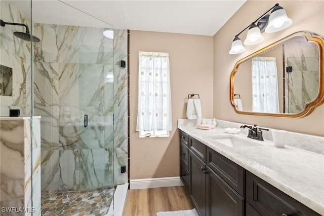 bathroom with a marble finish shower, baseboards, vanity, and wood finished floors