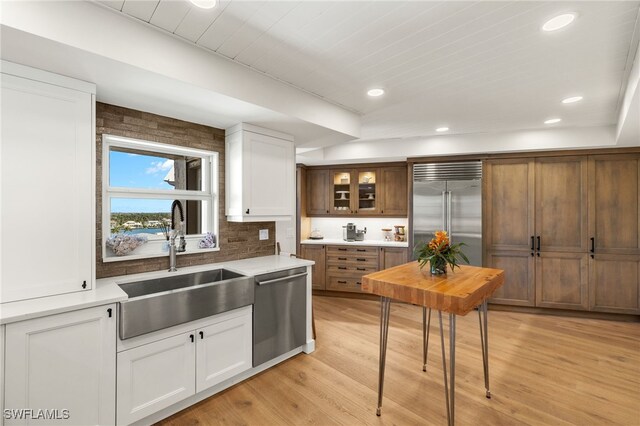 kitchen featuring light wood-type flooring, light countertops, white cabinets, appliances with stainless steel finishes, and a sink
