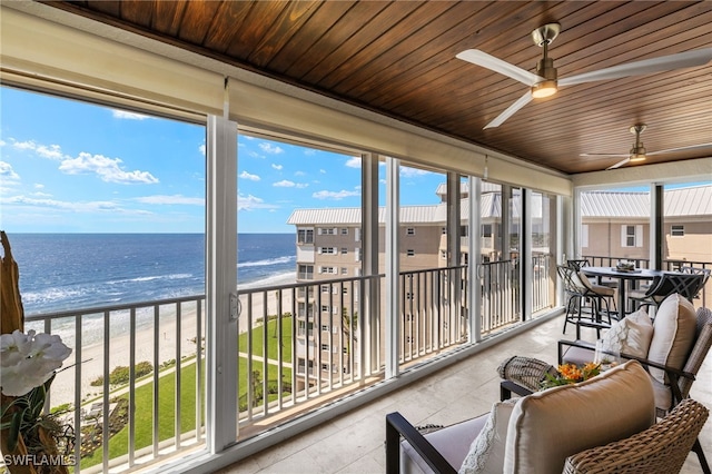 sunroom featuring tile patterned floors, a beach view, a ceiling fan, a water view, and wood ceiling