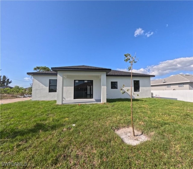 rear view of house with a yard, stucco siding, and fence