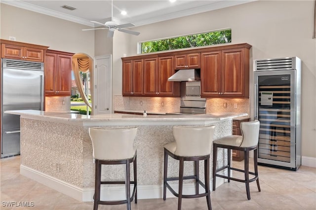 kitchen with light countertops, under cabinet range hood, visible vents, wine cooler, and stainless steel built in fridge