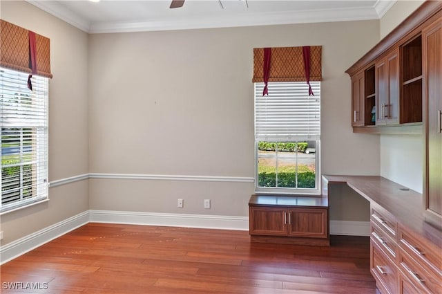 unfurnished room with built in desk, hardwood / wood-style floors, crown molding, and a healthy amount of sunlight