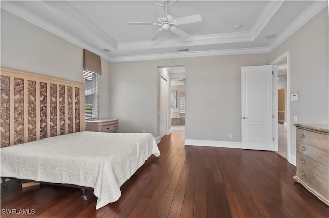 bedroom with dark wood-style floors, a tray ceiling, baseboards, and crown molding