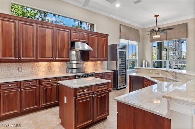 kitchen featuring range, a ceiling fan, under cabinet range hood, a center island with sink, and built in fridge