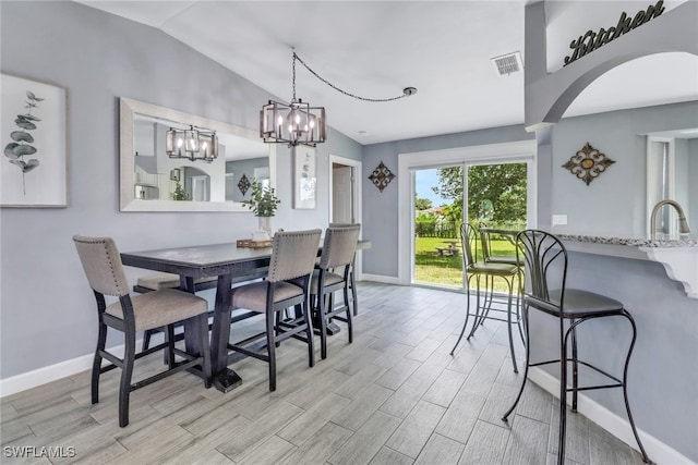 dining room featuring visible vents, baseboards, arched walkways, light wood-style floors, and vaulted ceiling