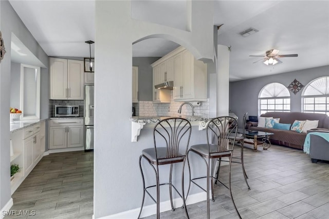 kitchen with visible vents, appliances with stainless steel finishes, light stone counters, and a breakfast bar area
