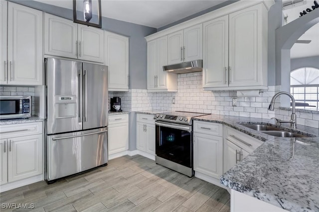kitchen featuring light stone countertops, arched walkways, under cabinet range hood, a sink, and stainless steel appliances