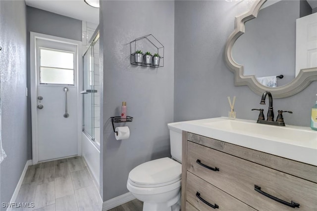 bathroom with combined bath / shower with glass door, vanity, baseboards, and toilet