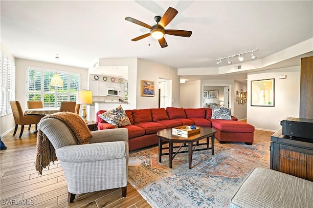 living area featuring light wood-style flooring, ceiling fan, baseboards, and rail lighting