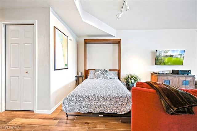 bedroom featuring wood finished floors, rail lighting, and baseboards
