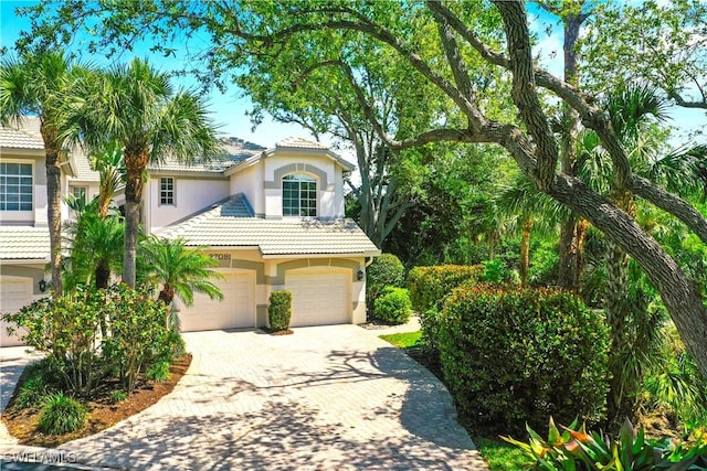 view of front of house featuring stucco siding, a tile roof, driveway, and a garage