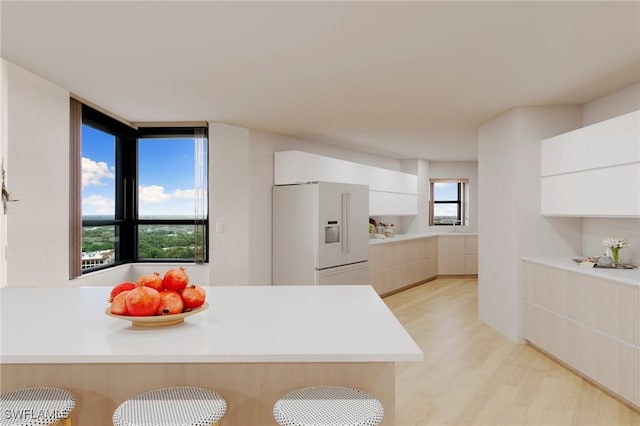 kitchen with light wood finished floors, modern cabinets, white refrigerator with ice dispenser, and light countertops