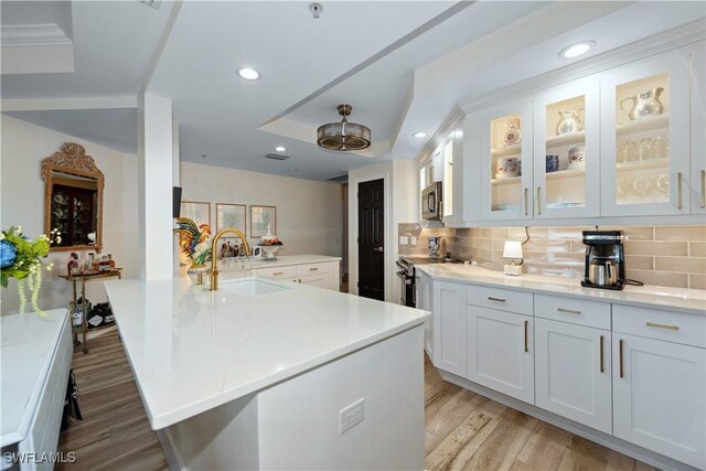 kitchen with a sink, stainless steel appliances, tasteful backsplash, light wood finished floors, and white cabinets