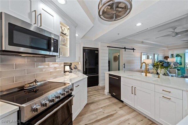 kitchen with light wood finished floors, decorative backsplash, black appliances, and a sink