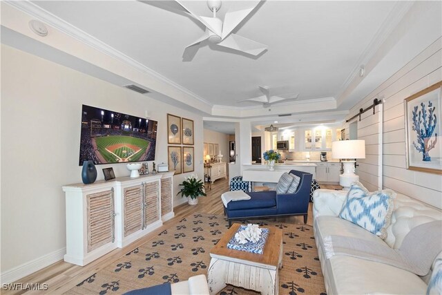 living area featuring light wood finished floors, a barn door, visible vents, and ceiling fan