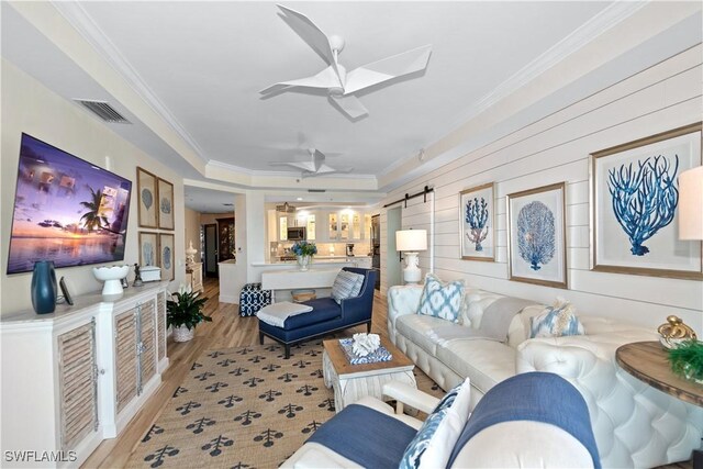 living room featuring ceiling fan, crown molding, a barn door, and light wood-type flooring