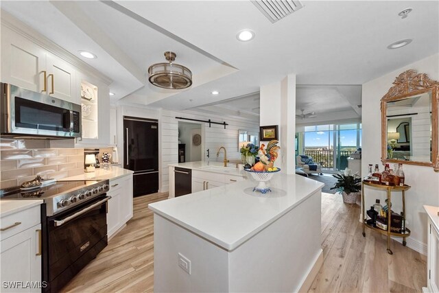 kitchen with a barn door, a sink, black appliances, light countertops, and tasteful backsplash