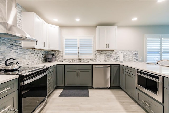 668 104th Ave N, Naples, FL 34108 - kitchen with wall chimney range hood, white cabinetry, a sink, light wood-style flooring, and stainless steel appliances
