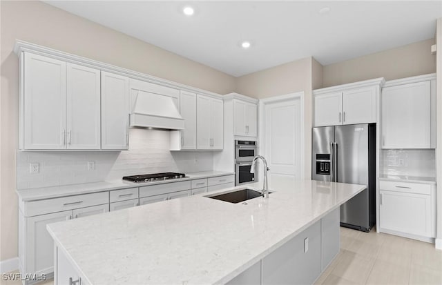 7060 Del Webb Oak Creek Blvd, North Fort Myers, FL 33917 - kitchen featuring appliances with stainless steel finishes, premium range hood, a sink, white cabinets, and a kitchen island with sink