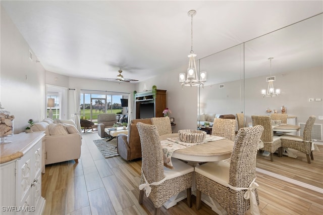 dining space with light wood-type flooring, ceiling fan with notable chandelier, and visible vents