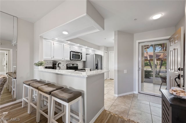 kitchen with tasteful backsplash, appliances with stainless steel finishes, a peninsula, white cabinetry, and light stone countertops