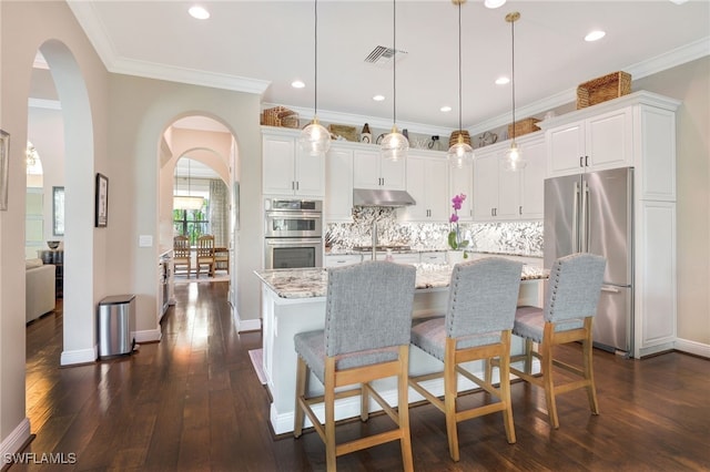 kitchen with dark wood finished floors, under cabinet range hood, stainless steel appliances, visible vents, and arched walkways
