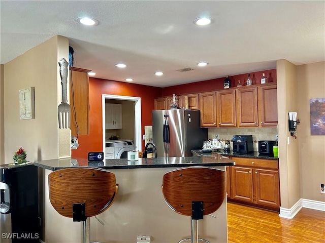 kitchen featuring a peninsula, freestanding refrigerator, dark countertops, brown cabinets, and a kitchen bar