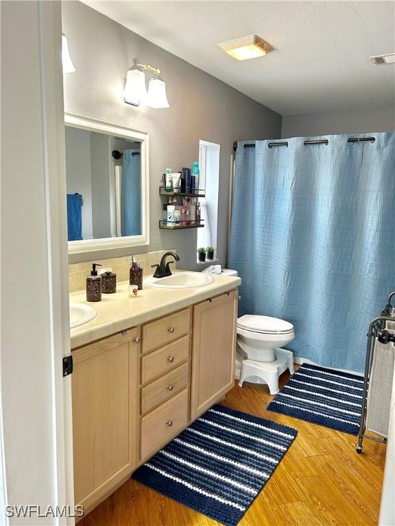 bathroom featuring visible vents, a sink, toilet, double vanity, and wood finished floors