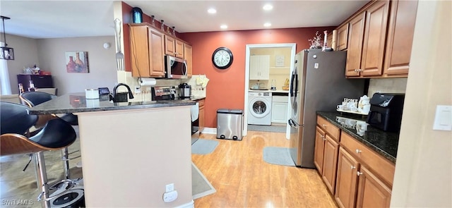 kitchen featuring a kitchen breakfast bar, light wood-type flooring, recessed lighting, washer / dryer, and stainless steel appliances