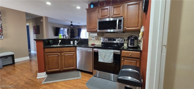kitchen featuring light wood-type flooring, a peninsula, dark countertops, decorative backsplash, and stainless steel appliances