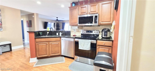 kitchen with ceiling fan, a peninsula, light wood-type flooring, appliances with stainless steel finishes, and a sink