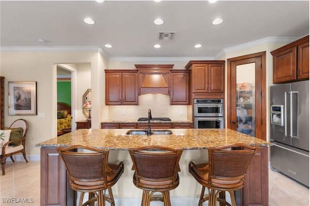 kitchen with visible vents, a sink, a kitchen island with sink, appliances with stainless steel finishes, and custom exhaust hood