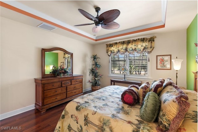 bedroom featuring a ceiling fan, a tray ceiling, baseboards, dark wood-style flooring, and visible vents