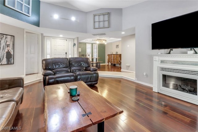 living area featuring high vaulted ceiling, baseboards, a glass covered fireplace, and wood finished floors