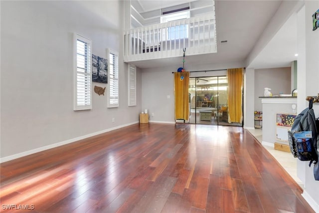 unfurnished living room with baseboards, wood finished floors, and a high ceiling