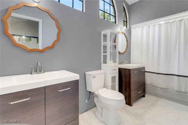 bathroom with two vanities, toilet, a towering ceiling, and a sink