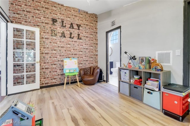 recreation room with brick wall, wood finished floors, and visible vents