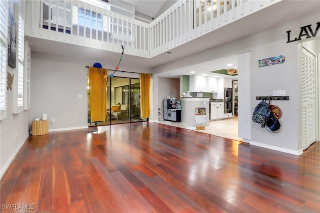 unfurnished living room with baseboards, wood finished floors, and a towering ceiling