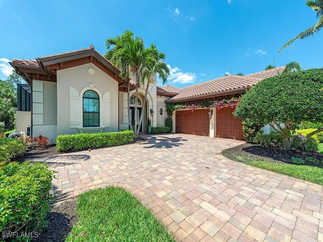 mediterranean / spanish-style house with an attached garage, a tiled roof, stucco siding, and decorative driveway