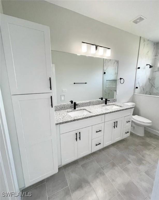 full bathroom featuring toilet, double vanity, a marble finish shower, and a sink