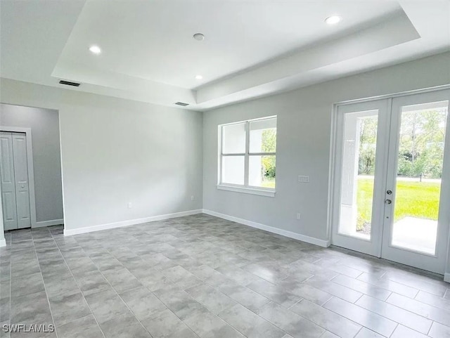 empty room featuring a tray ceiling, french doors, visible vents, and recessed lighting