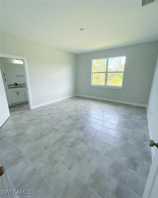 unfurnished bedroom featuring light tile patterned floors, baseboards, ensuite bathroom, and visible vents