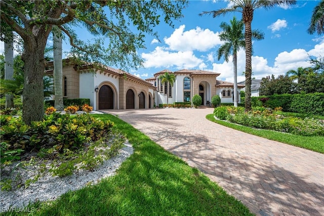 mediterranean / spanish-style home featuring a tile roof, decorative driveway, a garage, and stucco siding