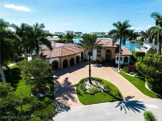 mediterranean / spanish house with a tile roof, curved driveway, a water view, and stucco siding