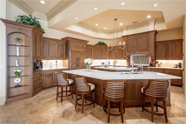 kitchen featuring tasteful backsplash, stone tile flooring, light countertops, ornamental molding, and a large island with sink